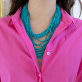 Person wearing a bright pink shirt and multi strand turquoise beaded necklace.