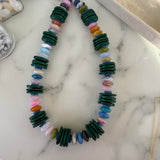 Colorful beaded necklace with thin, dark green ,wooden disc beads on a marble surface