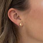 Model wearing a small brushed gold oval stud.