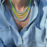 Necklace with blue and yellow beads worn by a person in a light blue denim shirt.