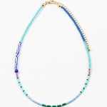 Dainty bead necklace in light blue, green and teal beads with some larger dark blue and striped beads.