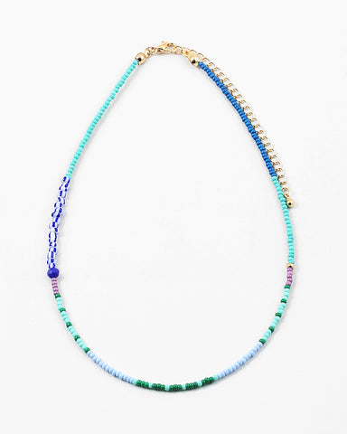 Dainty bead necklace in light blue, green and teal beads with some larger dark blue and striped beads.