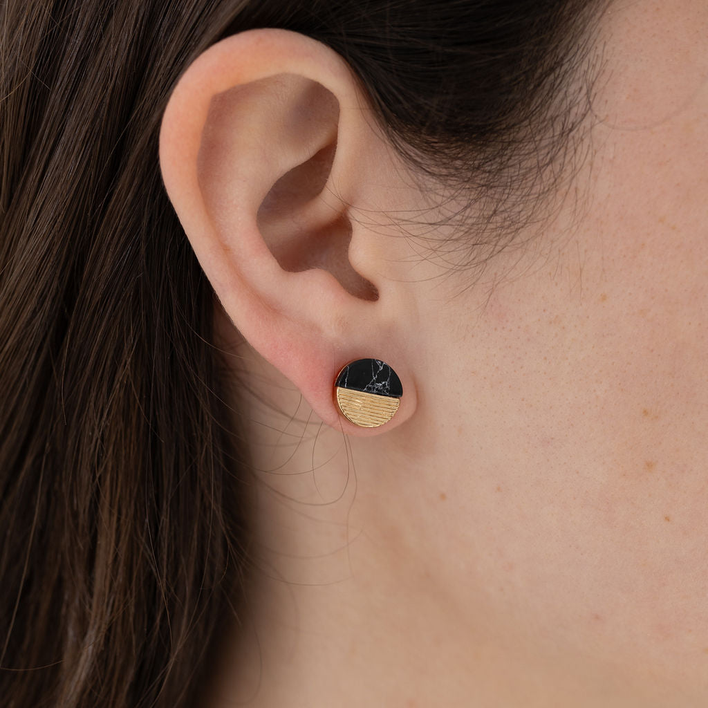 Picture of model wearing a small disc stud that is half black and half gold.