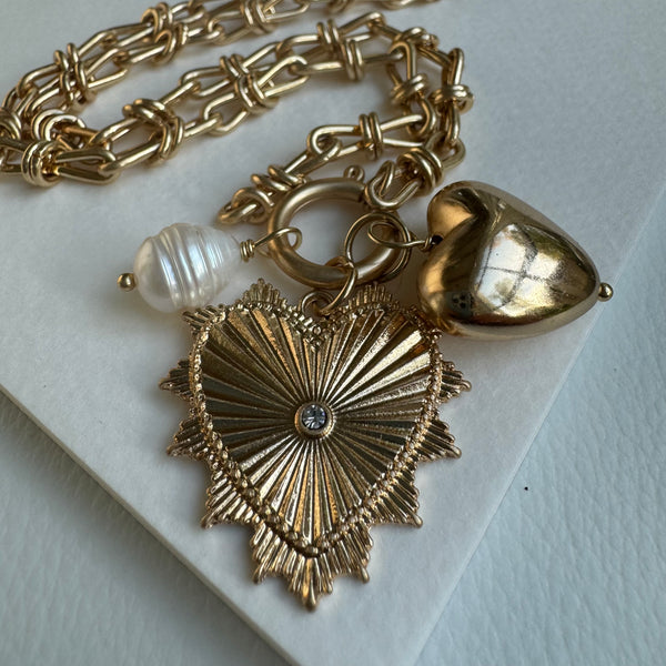 Picture of chunky gold chain linked charm necklace with a large gold heart pendant with a diamond at its center. Necklace has two charms, a mother of pearl bead and a large gold heart pendant.