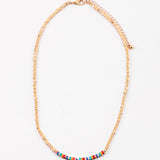 Dainty gold bead necklace with small red, yellow and turquoise beads at its center.