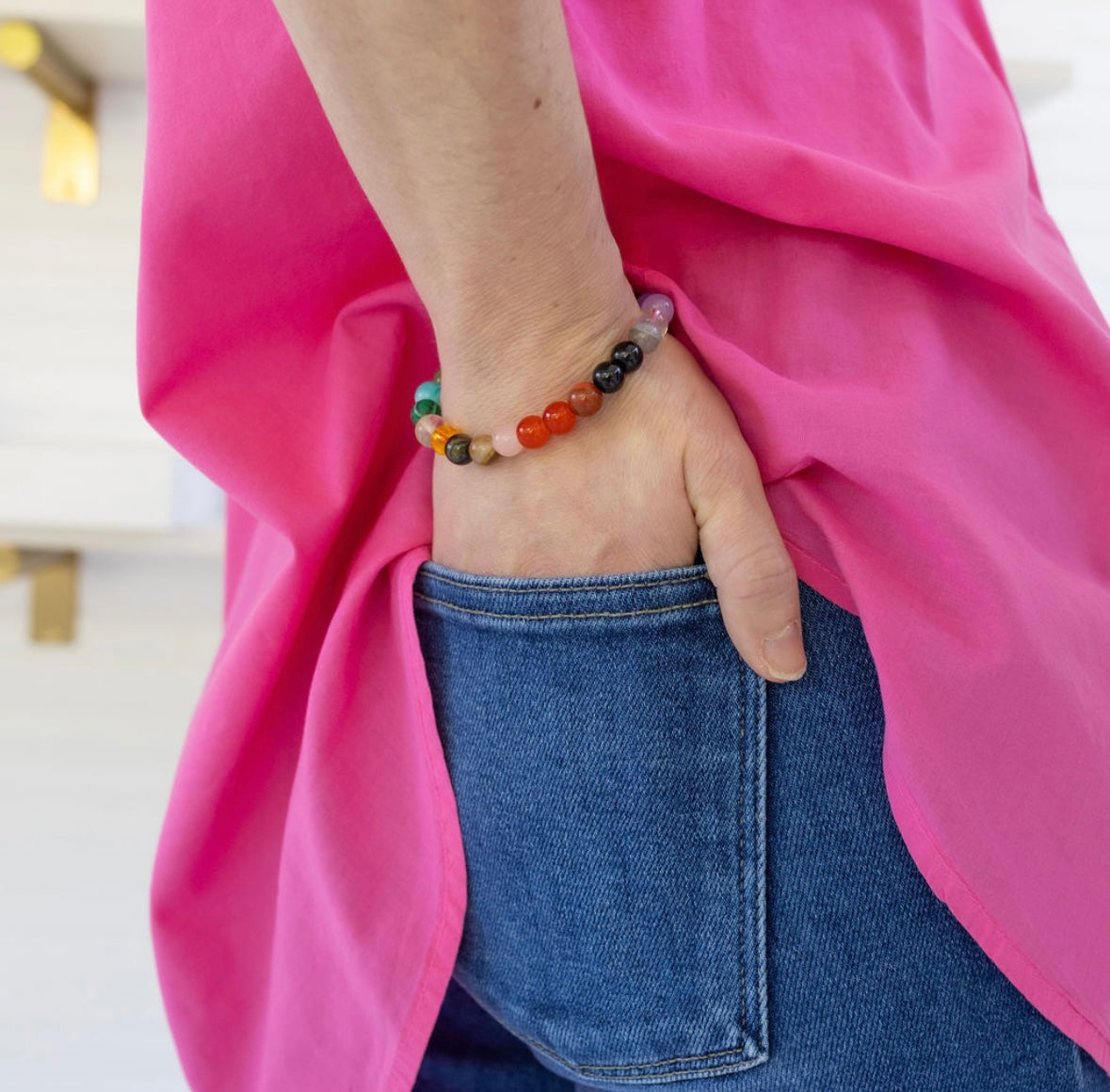 Person wearing a colorful beaded bracelet with a pink garment and blue jeans.