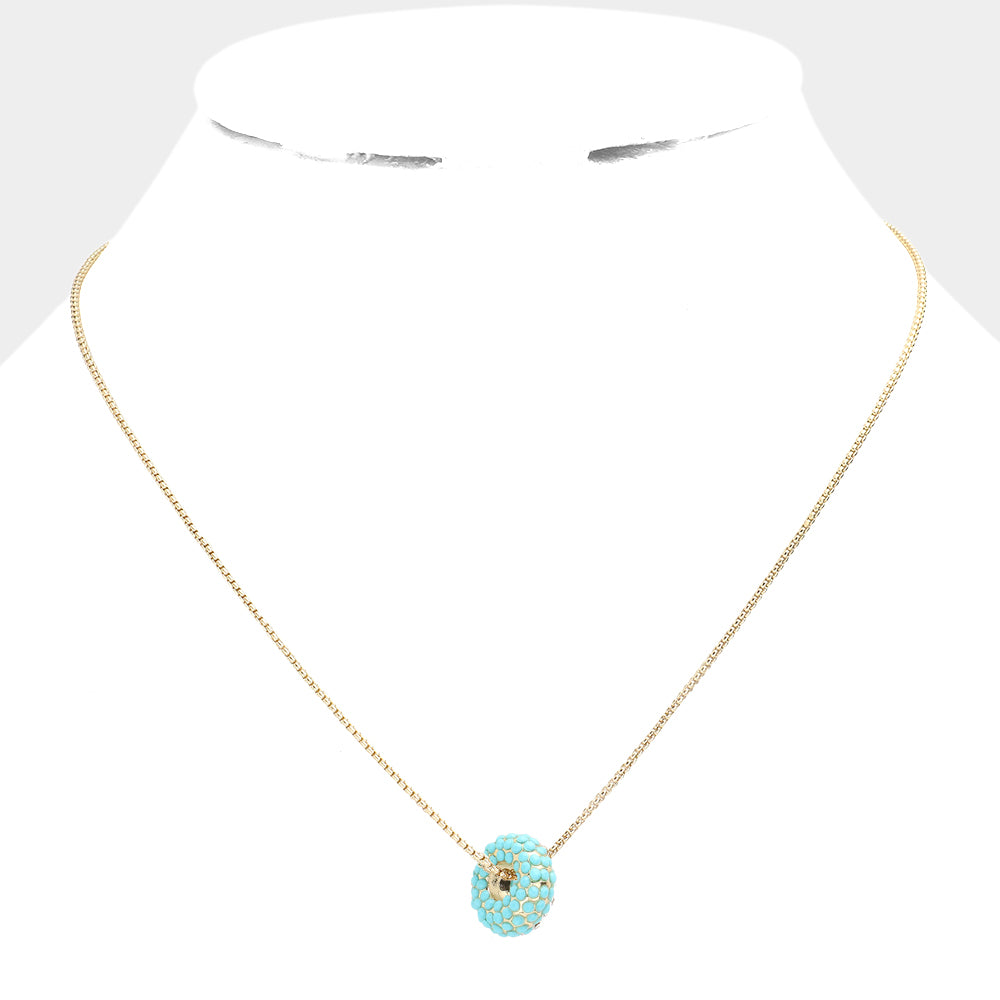 Gold necklace with a turquoise donut pendant on a white background