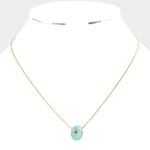 Gold necklace with a turquoise donut pendant on a white background