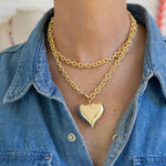 Gold chain necklace with a puffy heart pendant worn by a person in a denim shirt.