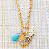Picture of gold toggle chain with a large gold heart pendant with a diamond at the center.  Also attached is a blue marbled teardrop bead and white elephant.