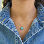 Person wearing a gold necklace with a turquoise elephant pendant and a denim jacket.