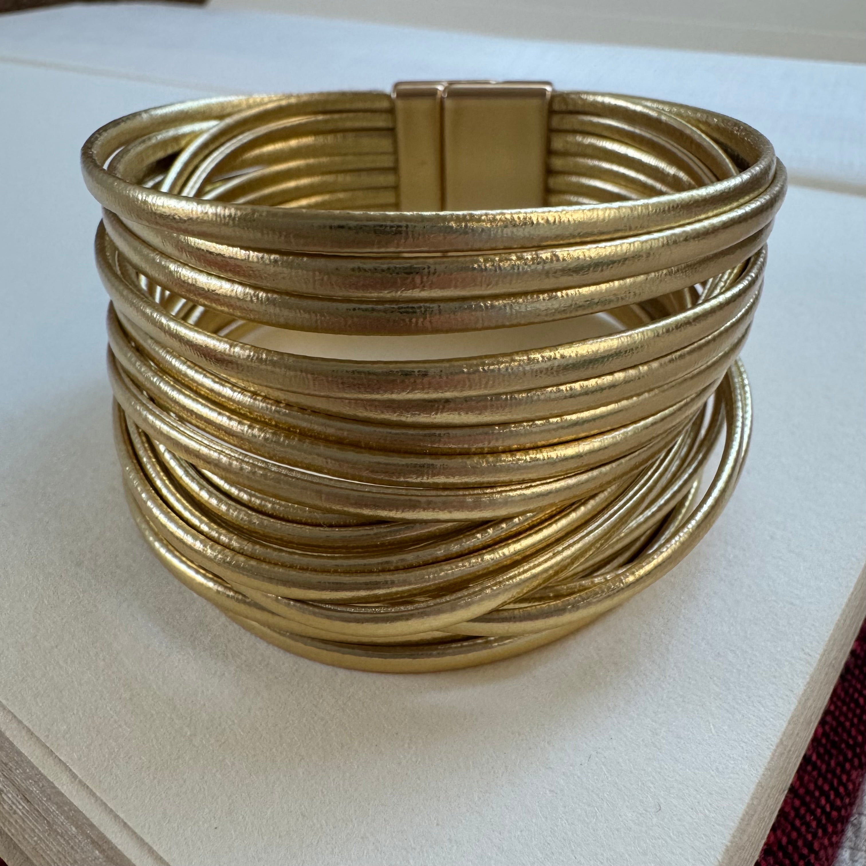 Cuff style bracelet made of many gold faux leather straps.