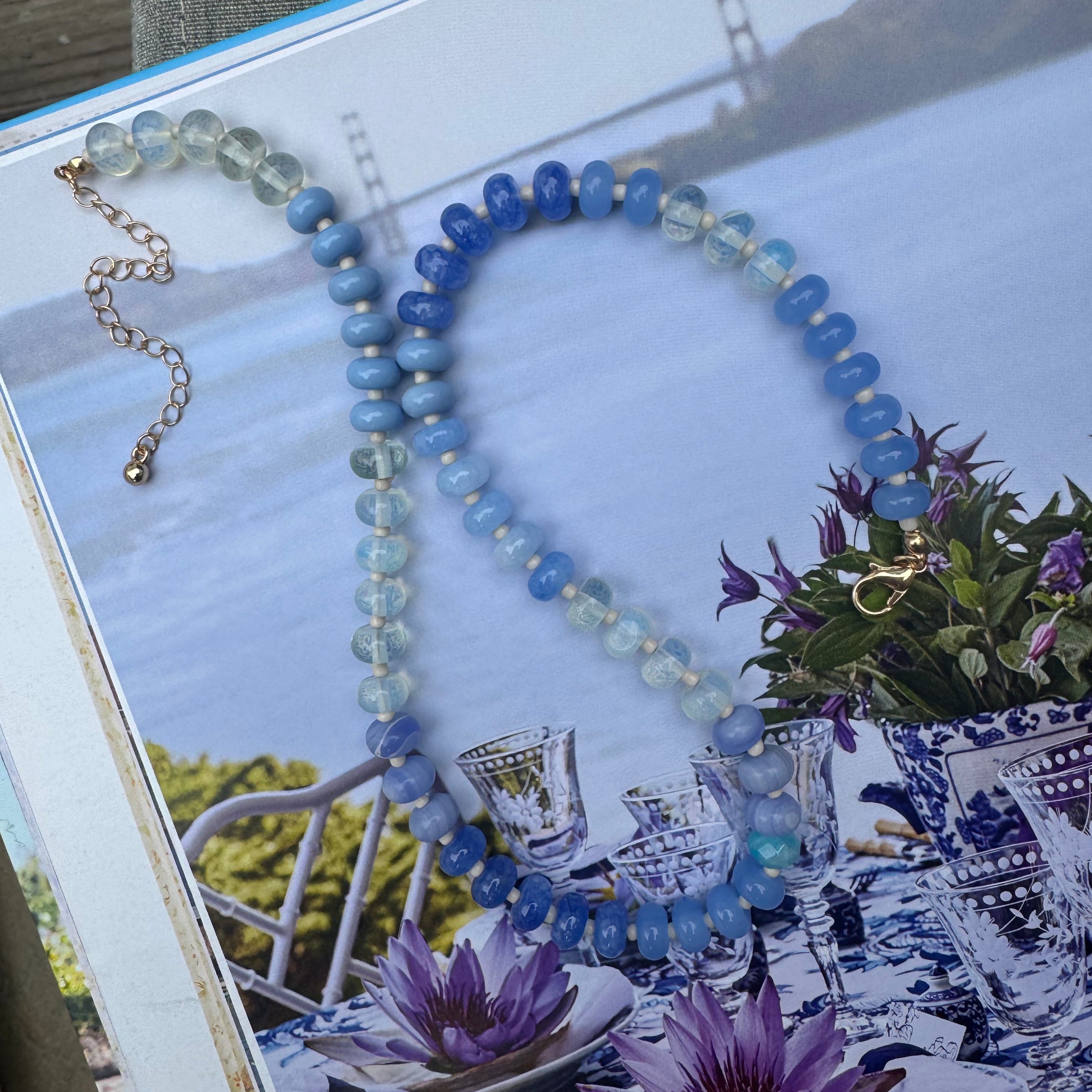 Beaded necklace of different shades of blues on a scenic book cover