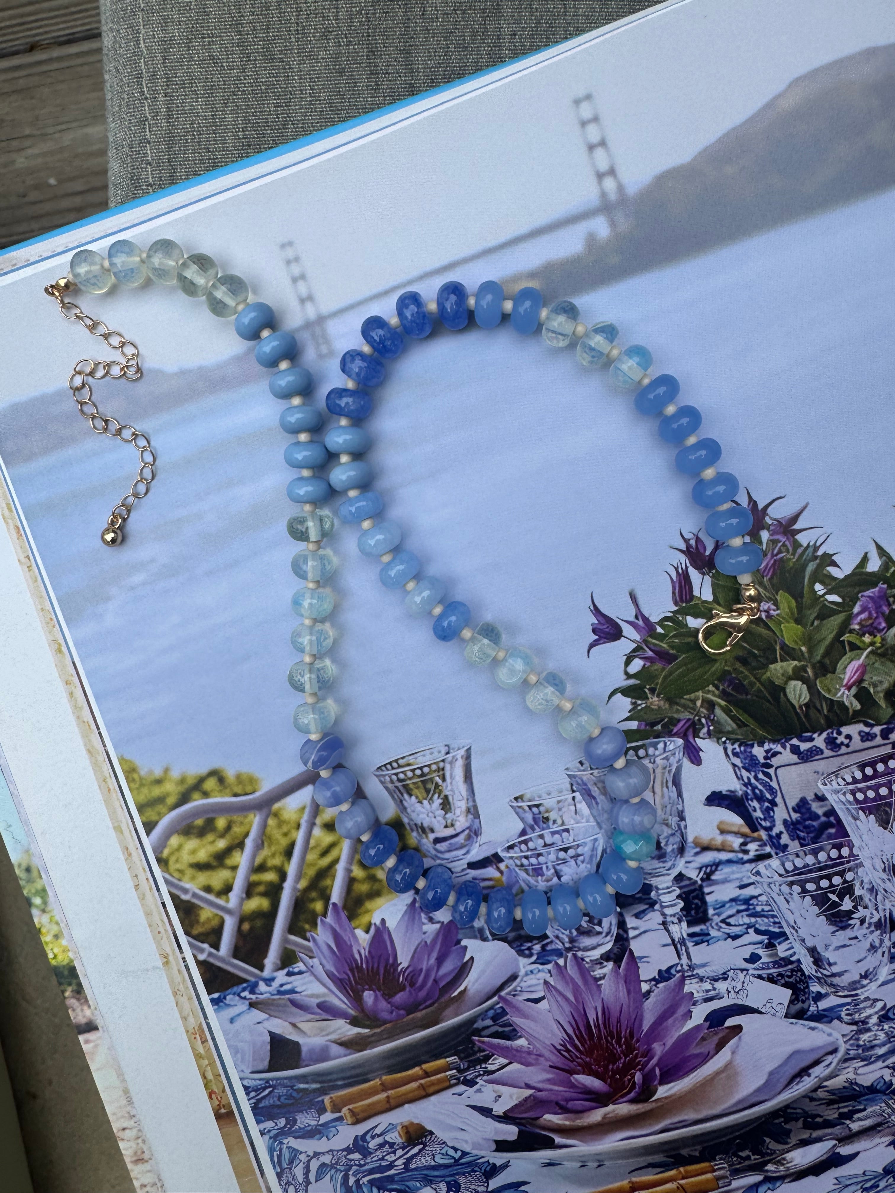 Beaded necklace of different shades of blues on a scenic book cover