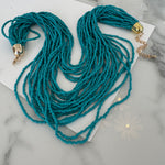 Picture of a necklace made out of multiple strands of teal beads with a large gold clasp.