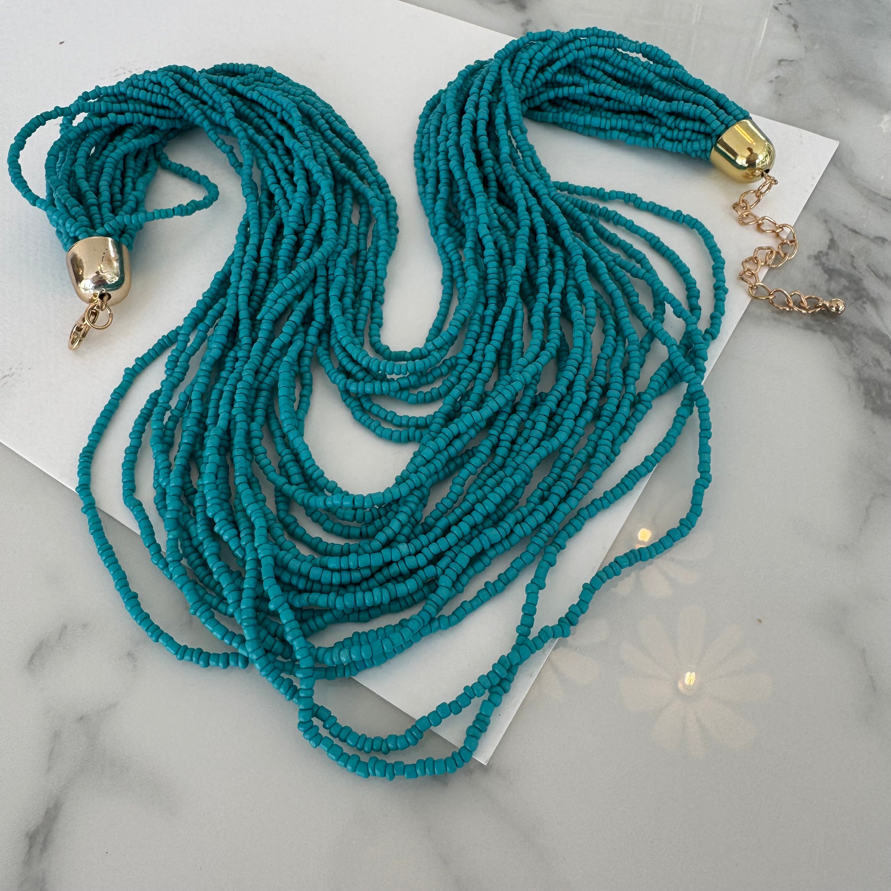 Picture of a necklace made out of multiple strands of teal beads with a large gold clasp.