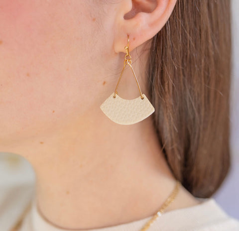 Picture of gold dangling earring with a cream colored leather strip.