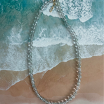 Clear bead necklace on a beach with waves in the background