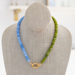 A beaded necklace with green and blue beads, featuring a gold-colored carabiner clasp, displayed on a mannequin.