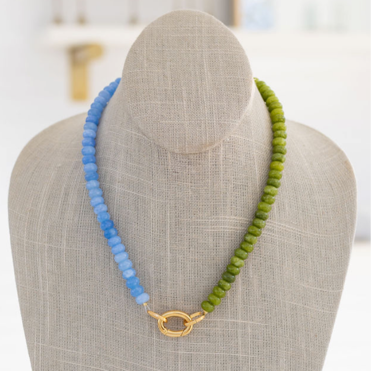 A beaded necklace with green and blue beads, featuring a gold-colored carabiner clasp, displayed on a mannequin.