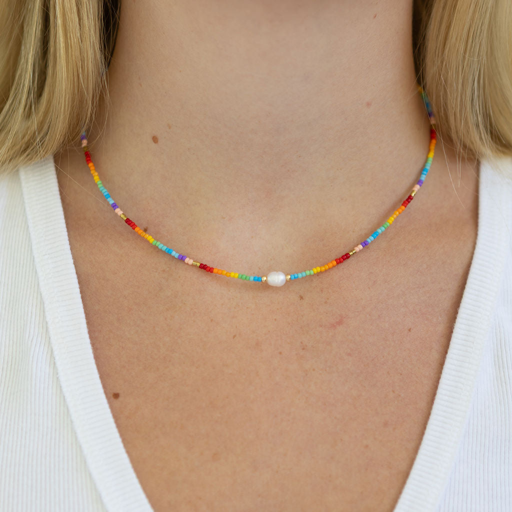 Colorful tiny beaded necklace with a central pearl pendant worn by a person with a white background