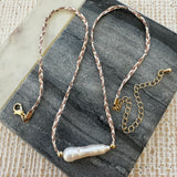 Picture of brown and white braided string necklace with large elongated fresh water pearl at its center.