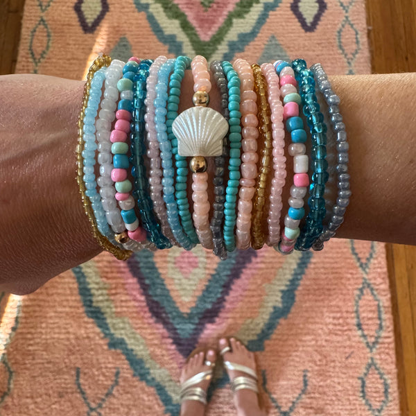 Picture of a woman's wrist wearing 16 different bracelets in Beach themed colors.  Bracelets are shades o white, corals, pinks, blues and amber.