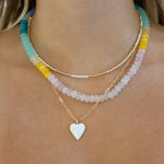 Necklace with white heart pendant and colorful beaded strands on a person's neck