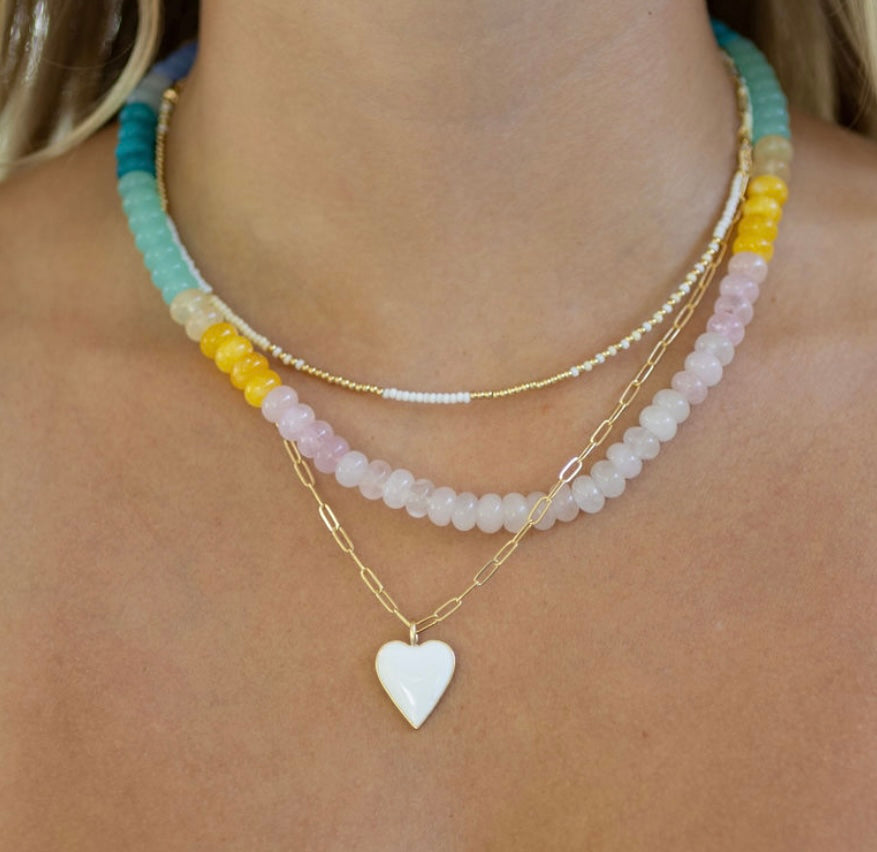 Necklace with white heart pendant and colorful beaded strands on a person's neck