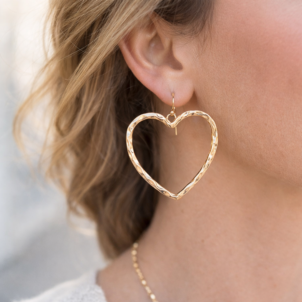 Gold heart-shaped earrings worn by a person with blurred background