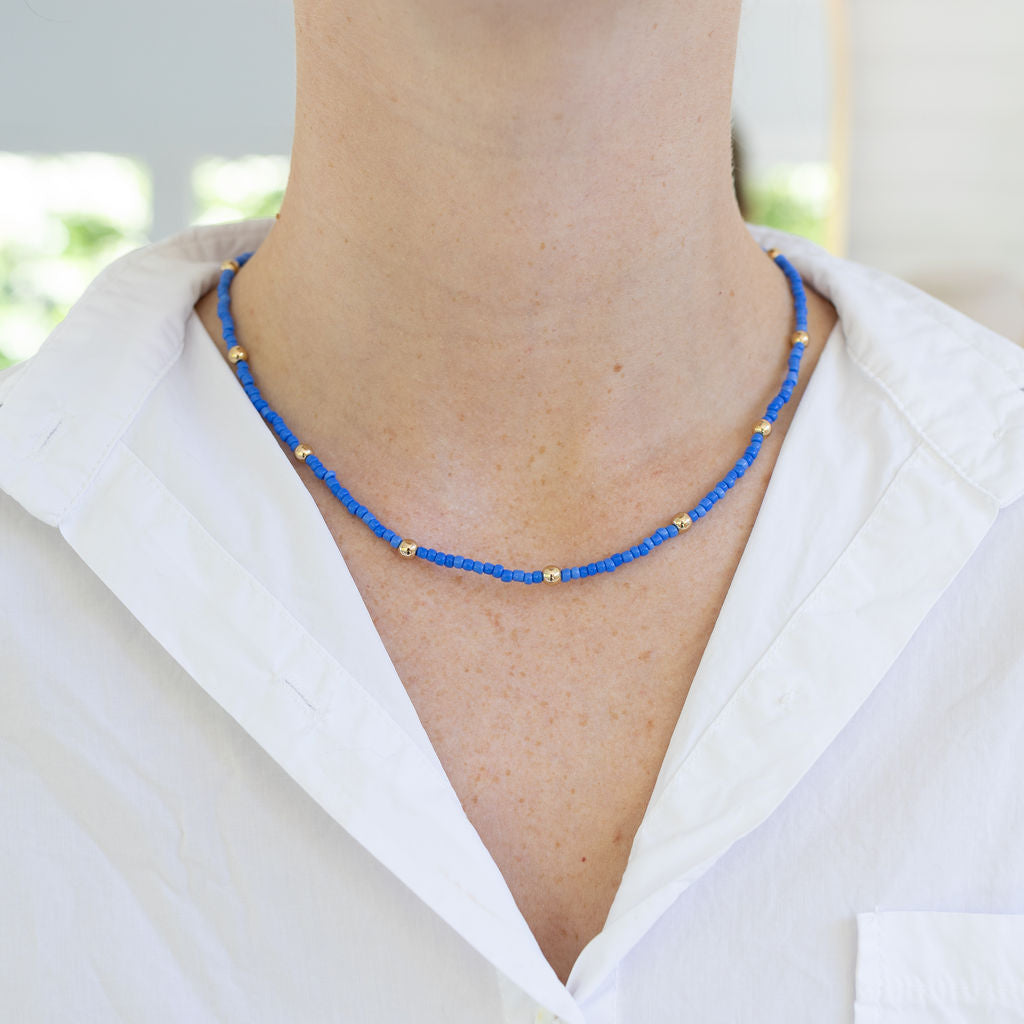 Picture of a dainty blue seed bead necklace with small gold spacers beads.