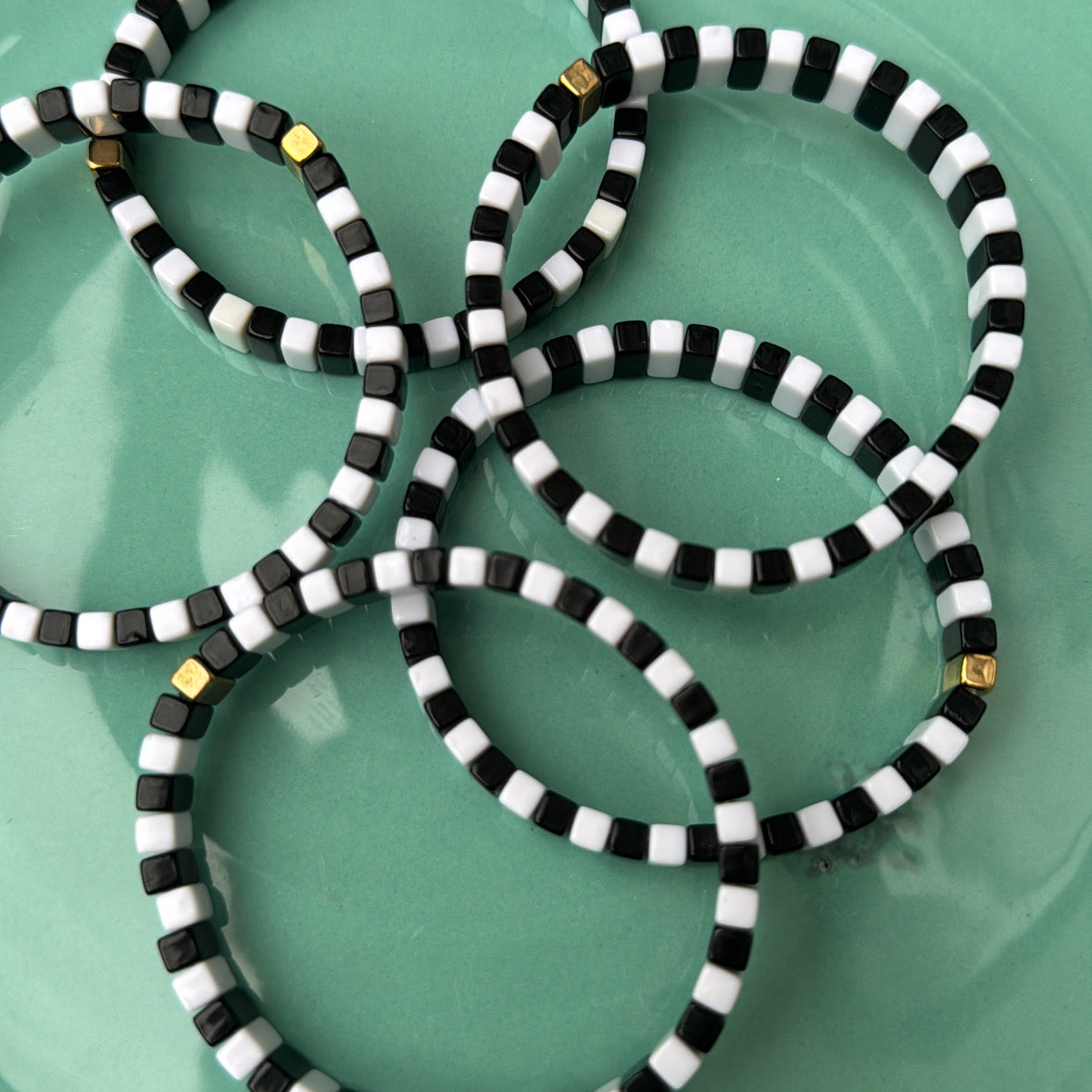 Picture of a green plate containing 5 black and white monochrome bracelets