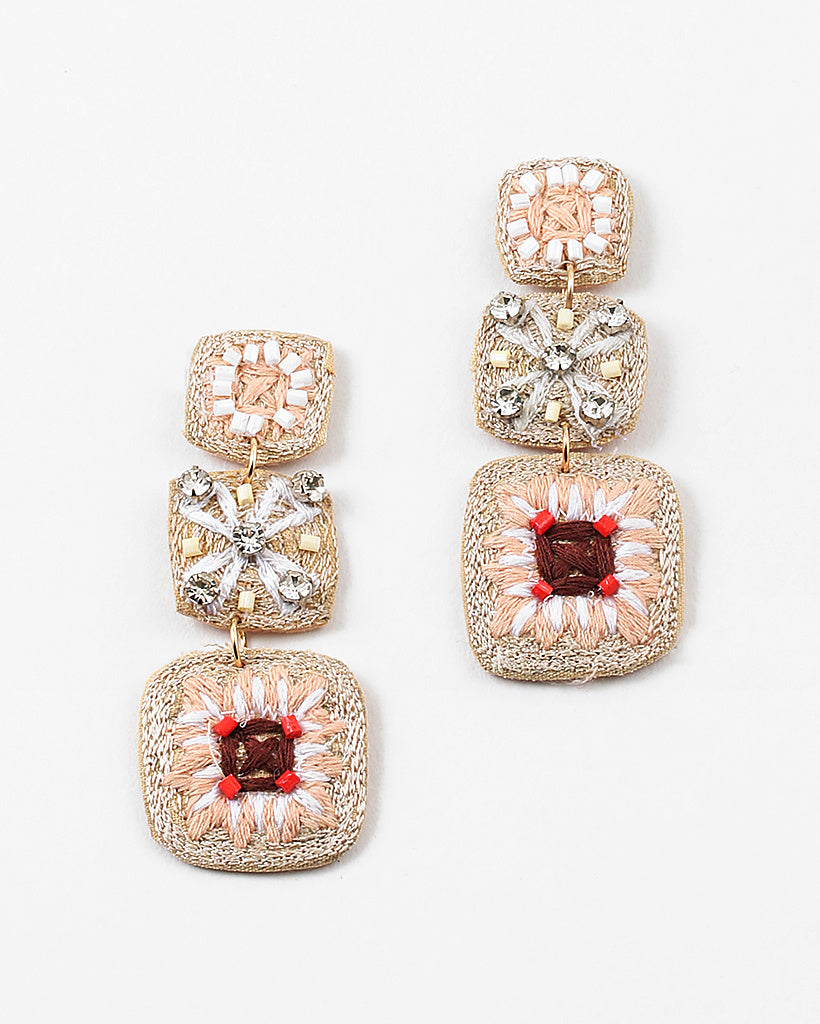A set of dangle earrings with three sections. Top square is woven in beige with white beads, the second is a beige woven square with white string and clear stones and the third section is a woven square with beige, white and brown strings and pink beads.