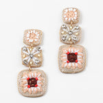A set of dangle earrings with three sections. Top square is woven in beige with white beads, the second is a beige woven square with white string and clear stones and the third section is a woven square with beige, white and brown strings and pink beads.