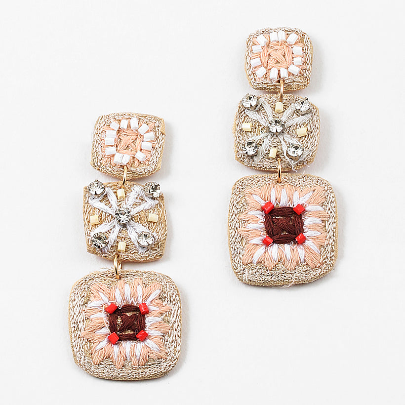 A set of dangle earrings with three sections. Top square is woven in beige with white beads, the second is a beige woven square with white string and clear stones and the third section is a woven square with beige, white and brown strings and pink beads.