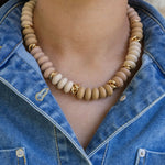 Necklace with beige beads and gold accents worn by a person in a denim jacket.