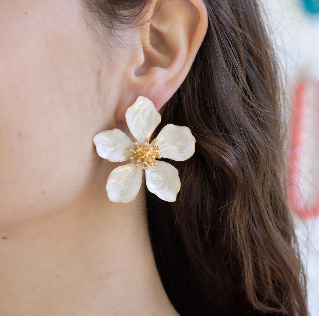 Large white floral earring worn by a person with brown hair.