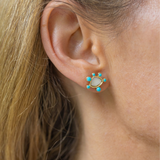 Girl wearing small earrings with a white/gold stone circular shape with tiny blue circular stones around it