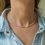Woman wearing a thin necklace with small pink/purple/gold beads and pearls