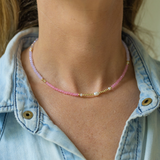Woman wearing a thin necklace with small pink/purple/gold beads and pearls