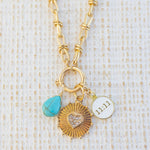 Picture of gold toggle chain with various charms attached.  One is a turquoise tear drop charm, gold textured disc with diamond heart in the center and white 11:11 disc.