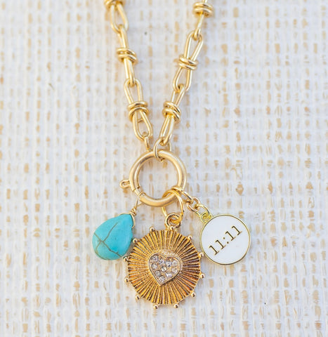 Picture of gold toggle chain with various charms attached.  One is a turquoise tear drop charm, gold textured disc with diamond heart in the center and white 11:11 disc.