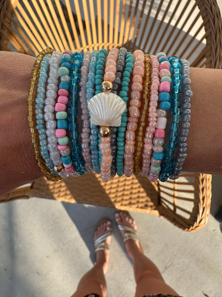 Picture of a woman's wrist wearing 16 different bracelets in Beach themed colors.  Bracelets are shades o white, corals, pinks, blues and amber.