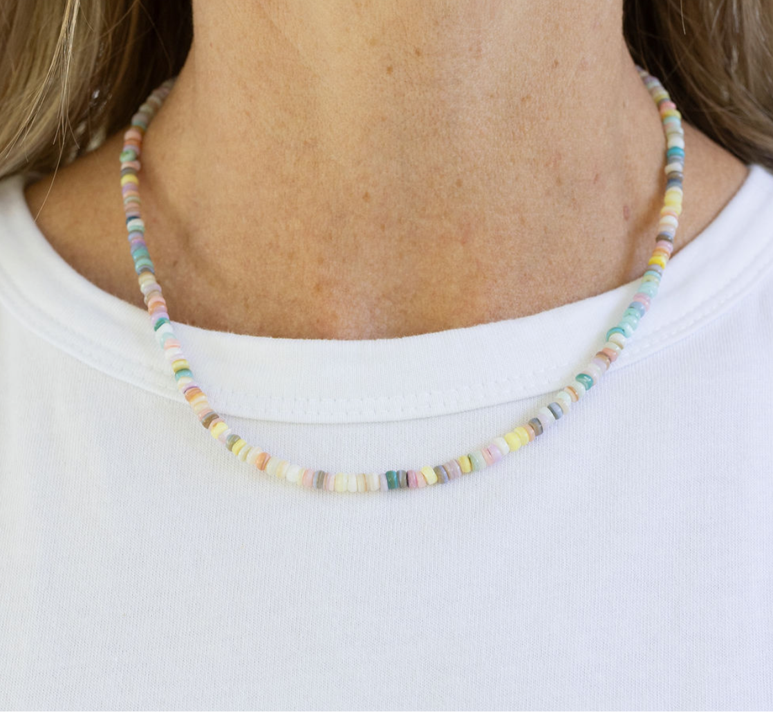 Picture of a woman's neck displaying a small white, beige and gray stone bead necklace.