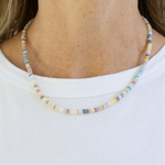 Picture of a woman's neck displaying a small white, beige and gray stone bead necklace.