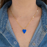 Person wearing a gold chain necklace with a blue heart pendant, against a denim background.