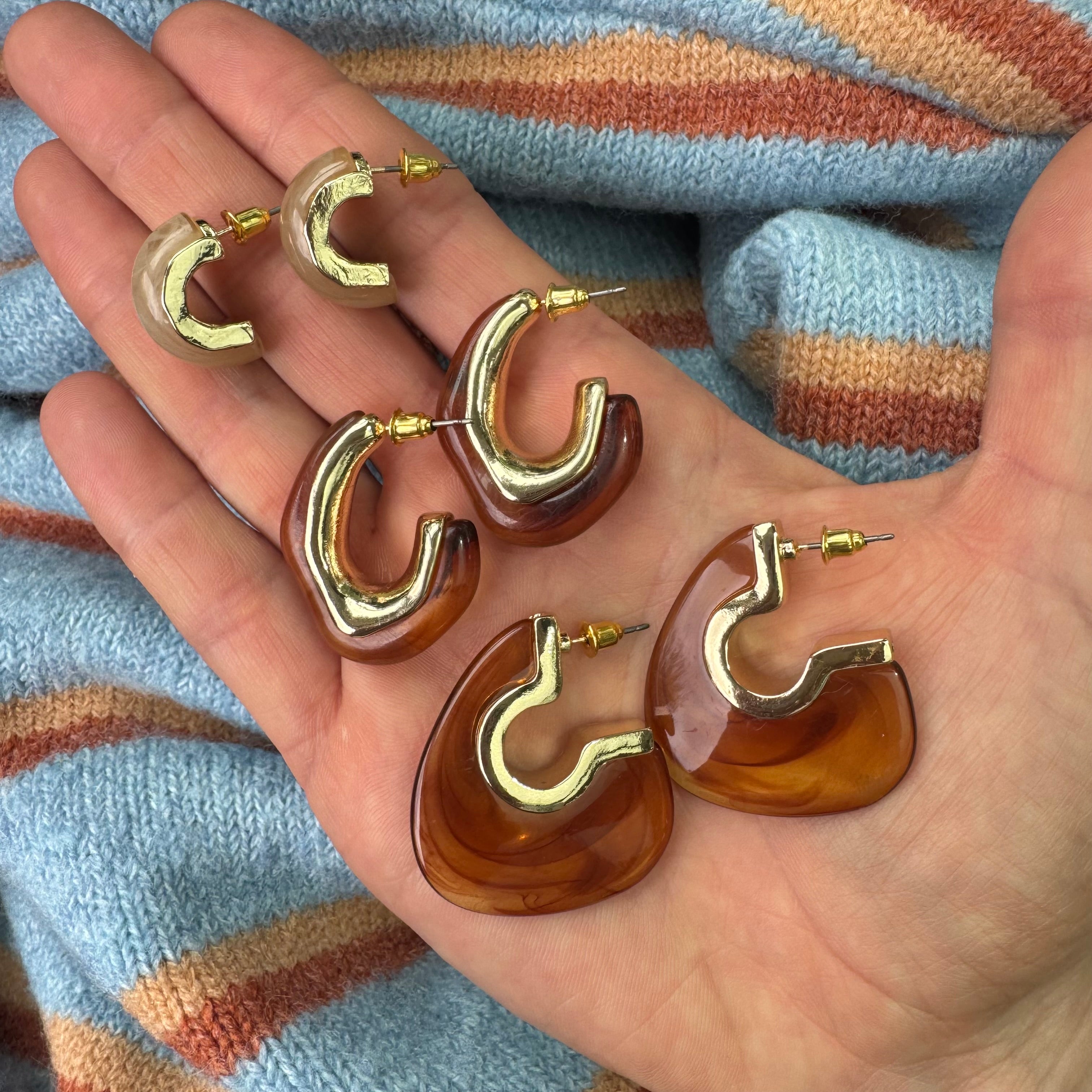 Gold and amber hoop earrings held in a hand with a striped fabric background