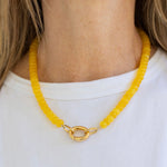 Yellow beaded necklace with a gold carabiner clasp worn by a person on a white background