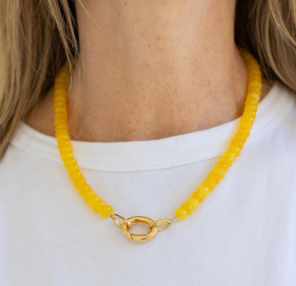Yellow beaded necklace with a gold carabiner clasp worn by a person on a white background