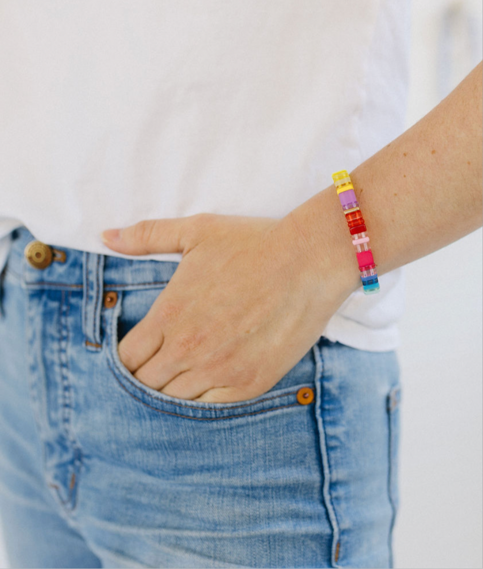 Picture of a woman with her hand in her pocket. She is wearing a beaded bracelet in yellows, purples, reds and blues.